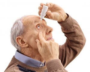 Elderly man applying eye drops isolated on white background