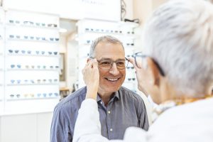 Happy mature man trying on glasses in optical shop.