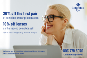 A smiling woman in tortoiseshell glasses rests her chin on her hand. Columbia Eye offer: 20% off your first pair of complete prescription glasses, 10% off lenses on a second pair.